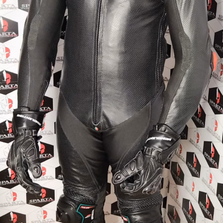 Pilota in piedi con tuta racing nera integrale SPARTA, guanti abbinati e protezioni su spalle, ginocchia e gomiti, su sfondo brandizzato abbigliamento moto - Personalizzato BeSparta Verona